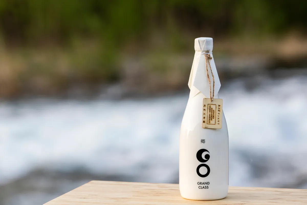 GO GRANDCLASS Uonuma Koshihikari Edition bottle by Tsunan Sake Brewery, on wood beside a flowing river